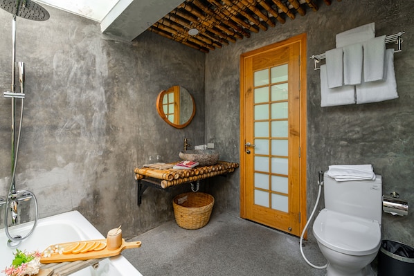 Une salle de bain avec une porte en bois, des toilettes blanches, un lavabo avec un receveur en pierre, un miroir et une douche.