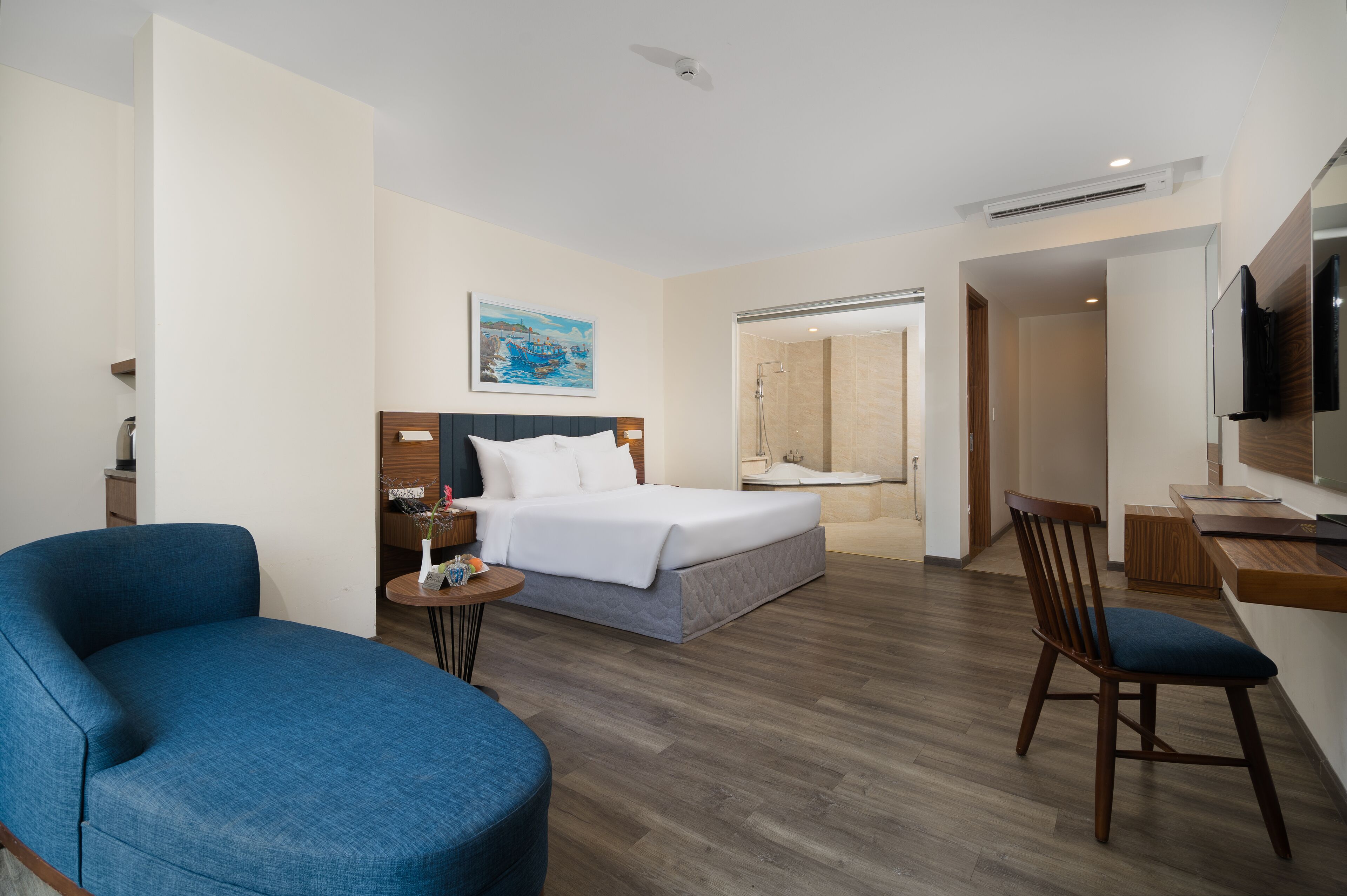 A hotel room with a bed, a desk, a chair, a small table, and a shower area.