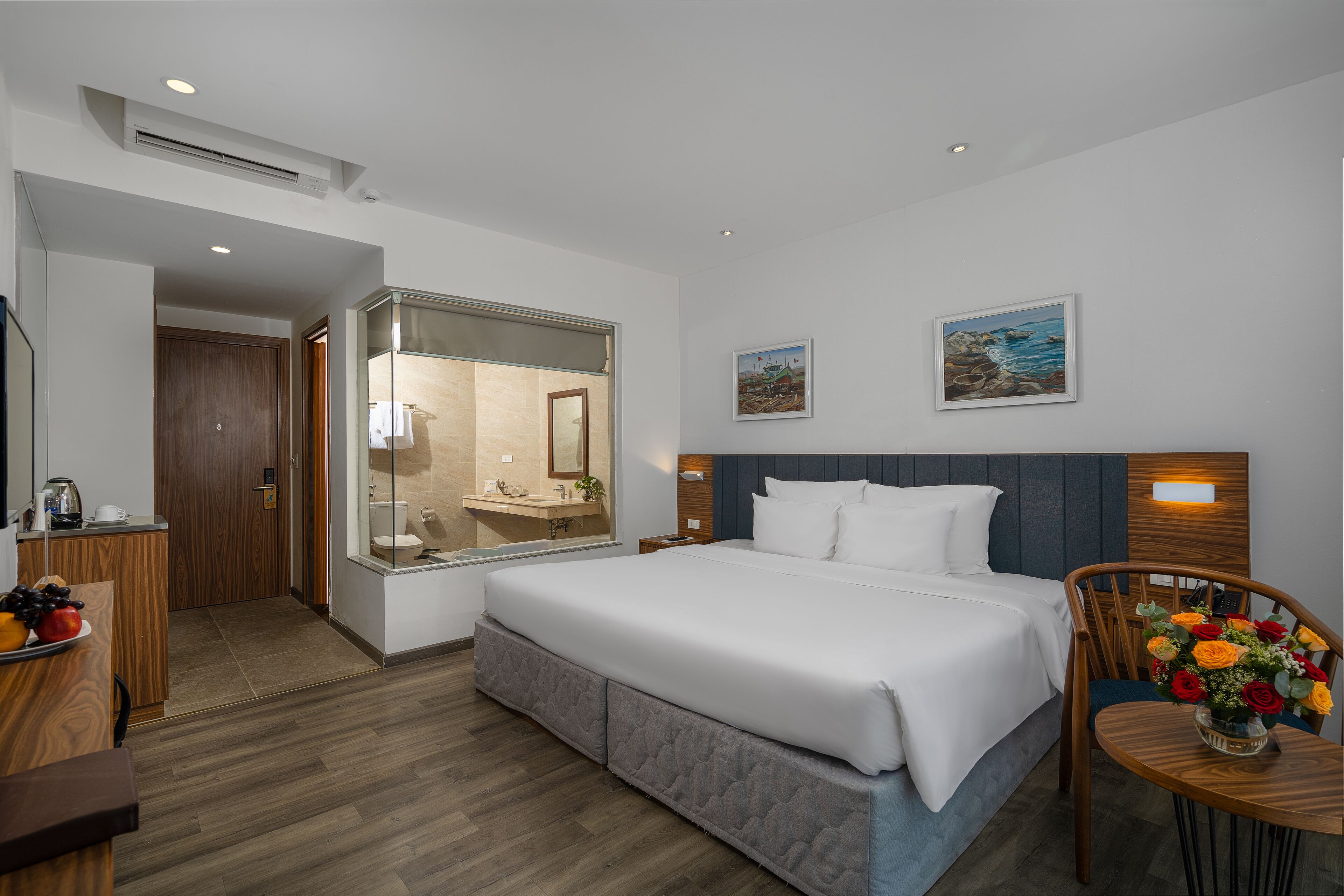 Een moderne hotelkamer met een groot bed, een houten bureau, een badkamer met een glazen douchewand en een zithoek met een stoel en tafel.