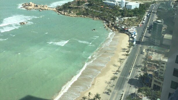 An aerial view of a coastal area with a beach, a road, and buildings. - Hoang Ky Hotel (Bac Nha Trang)