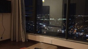 A room with a large window overlooking a cityscape at night, a wooden table, and a remote control on it. - Hoang Ky Hotel (Bac Nha Trang)