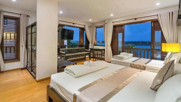A hotel room with a large bed, a TV, a balcony with a view, and a desk with a chair. -  B'Lan Riverside Villa (Da Nang)