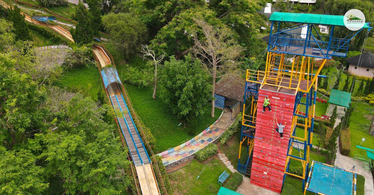 Vista aérea de un parque con montañas rusas, una estructura de escalada roja y azul, y abundante vegetación.
