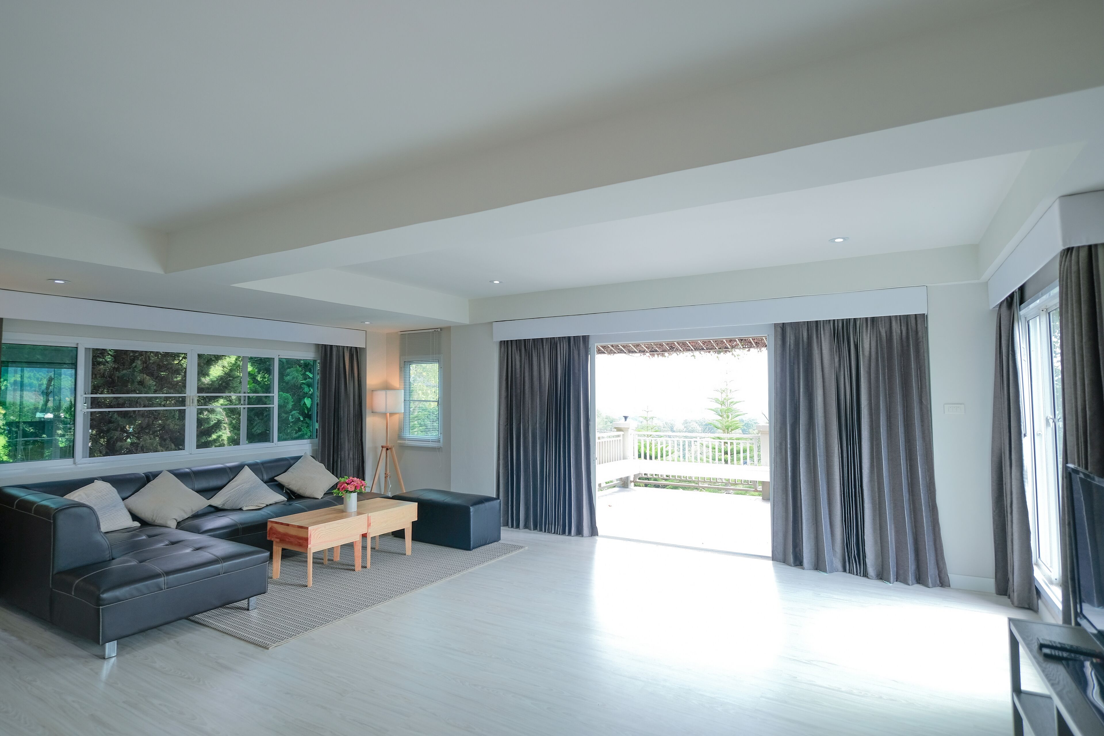 A spacious living room with a dark sofa, a wooden coffee table, and a large window with curtains.