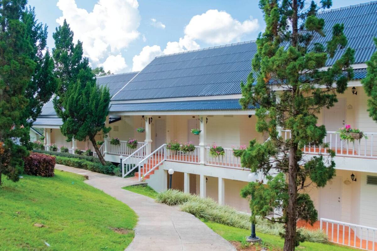 A building with a covered walkway, multiple balconies with hanging flower baskets, and a well-maintained lawn.
