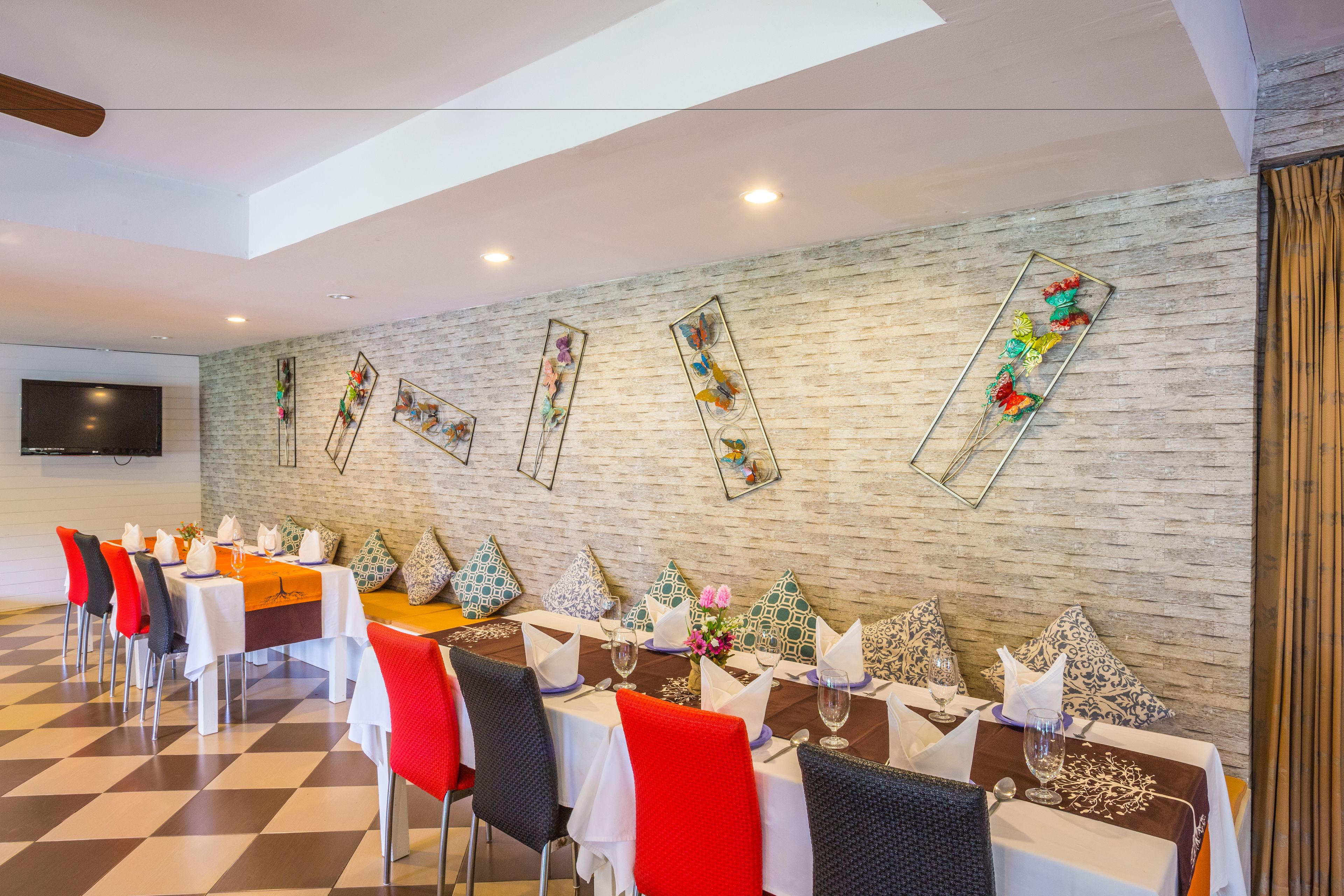 Un comedor con mesas dispuestas para el servicio, un televisor de pantalla plana en la pared y un suelo a cuadros.