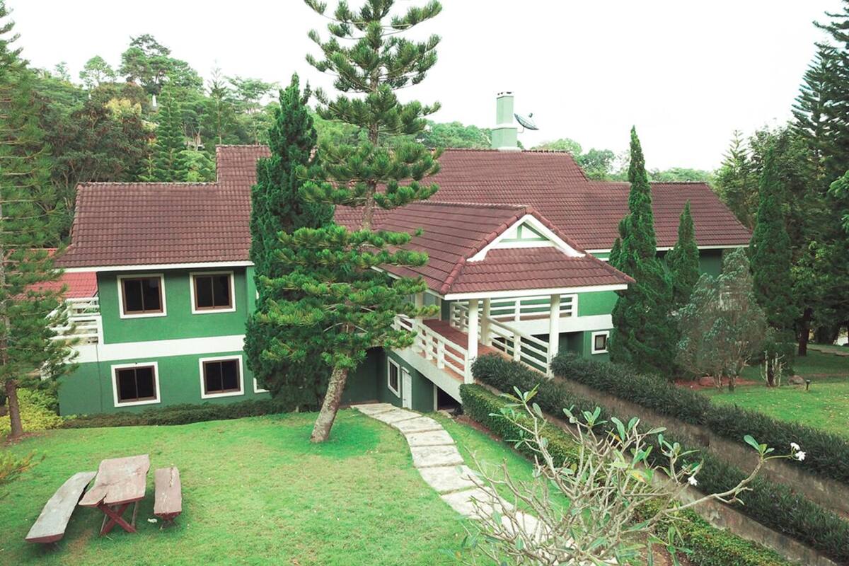 A two-story house with a red-tiled roof, a green exterior, and a white balcony.