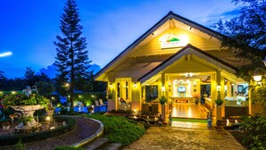 A well-lit hotel entrance with a covered porch, outdoor seating, and a landscaped garden area.