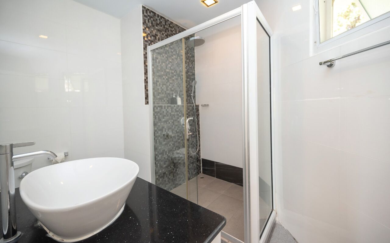 A modern bathroom with a freestanding white sink, a glass-enclosed shower, and a black countertop.