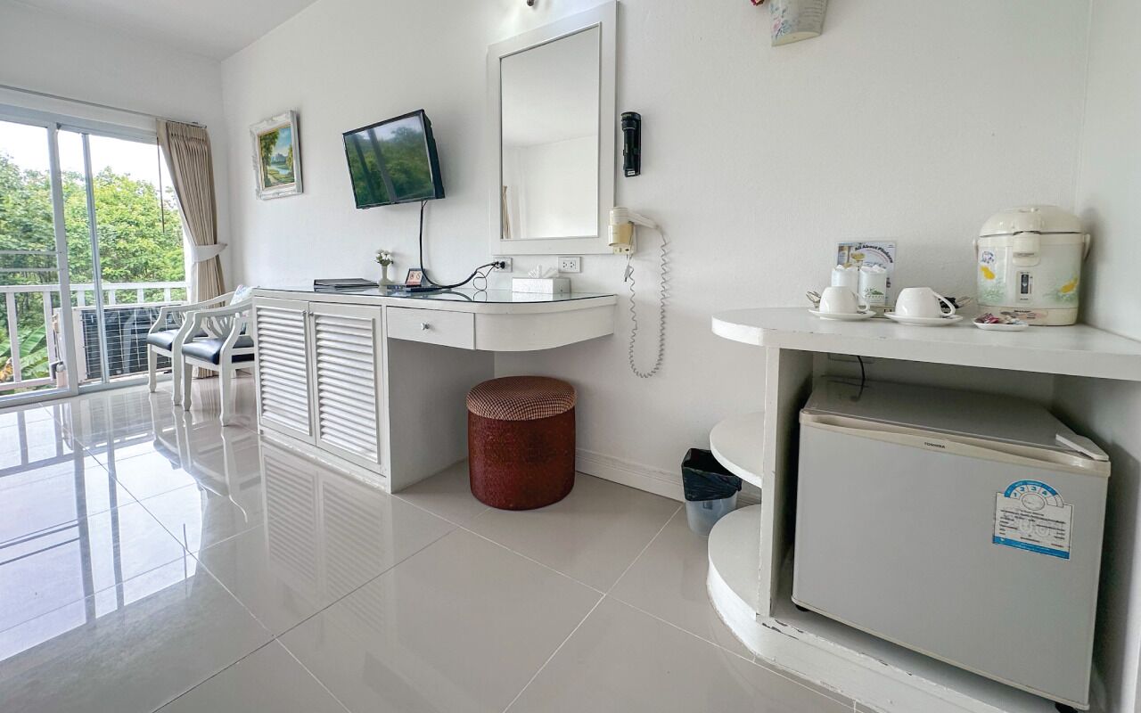 Habitación de hotel moderna con balcón, escritorio con computadora, televisor de pantalla plana, teléfono, cafetera y refrigerador.