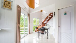 A spacious, well-lit room with a staircase leading to an upper level, a dining area with chairs and a table, and a door with a decorative sign.