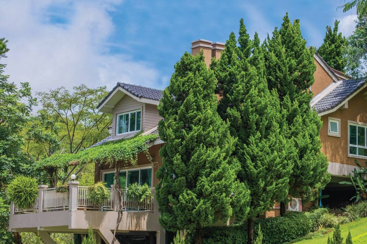 A two-story house with a balcony, surrounded by lush greenery and trees.