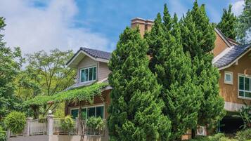 A two-story house with a balcony, surrounded by lush greenery and trees.