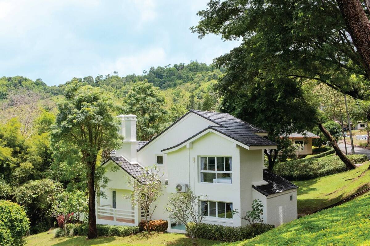A two-story house with a white exterior, surrounded by lush greenery and trees.