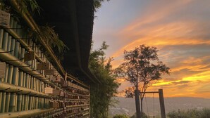 A pathway leading to a building with a bamboo fence and a view of a sunset.