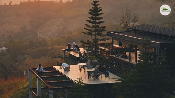 A modern outdoor dining area with tables and chairs, surrounded by lush greenery and hills in the background.