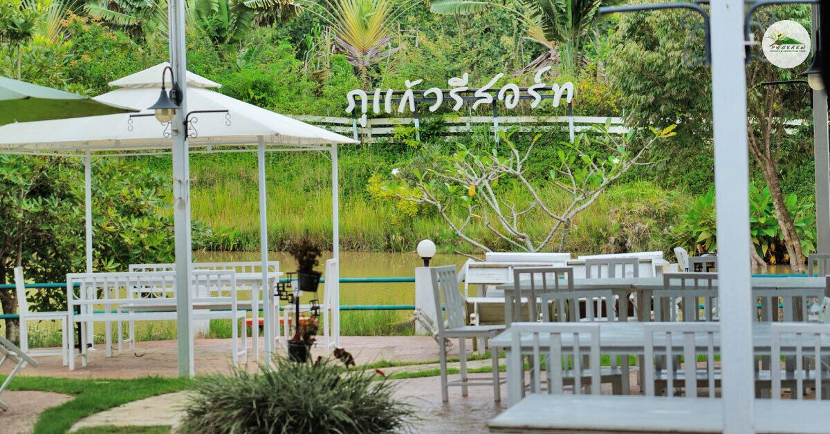 A covered outdoor seating area with white furniture and a white fence, surrounded by lush greenery.