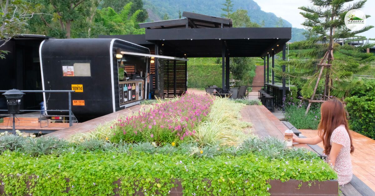 Una zona de estar al aire libre de estilo moderno con estructura negra, posiblemente un quiosco o bar, rodeada de abundante vegetación y una terraza de madera.