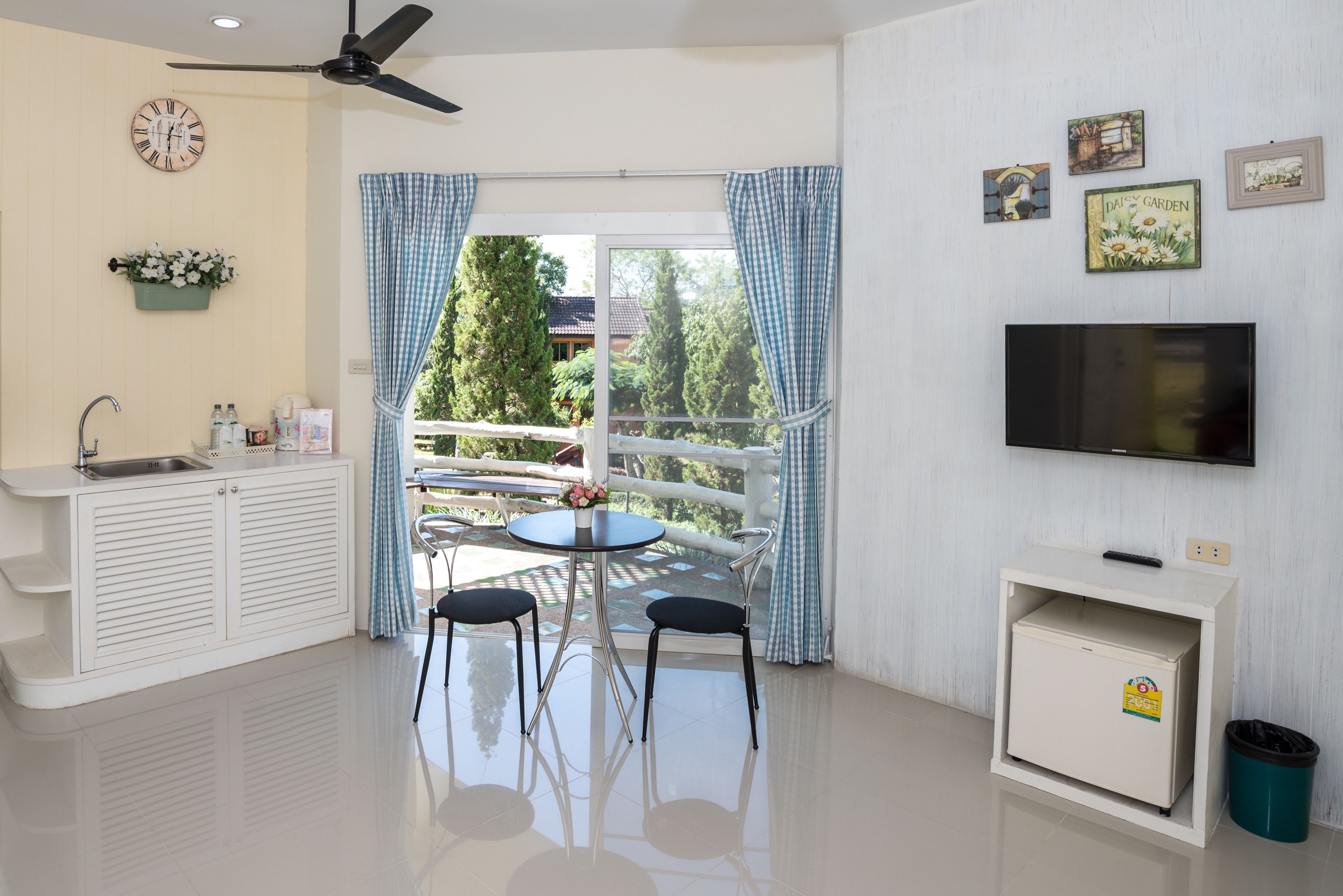A modern kitchen with a built-in sink, a dining area with two chairs, a ceiling fan, and a TV on a stand.