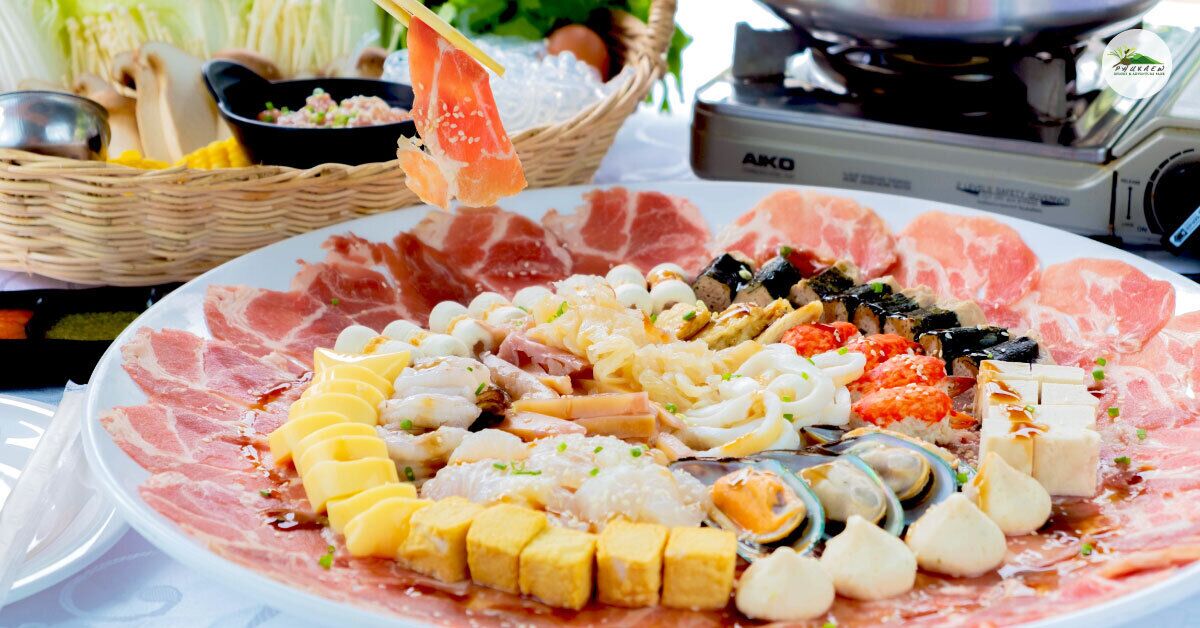 A variety of sushi and sashimi on a plate, with a basket of condiments and a portable stove in the background.