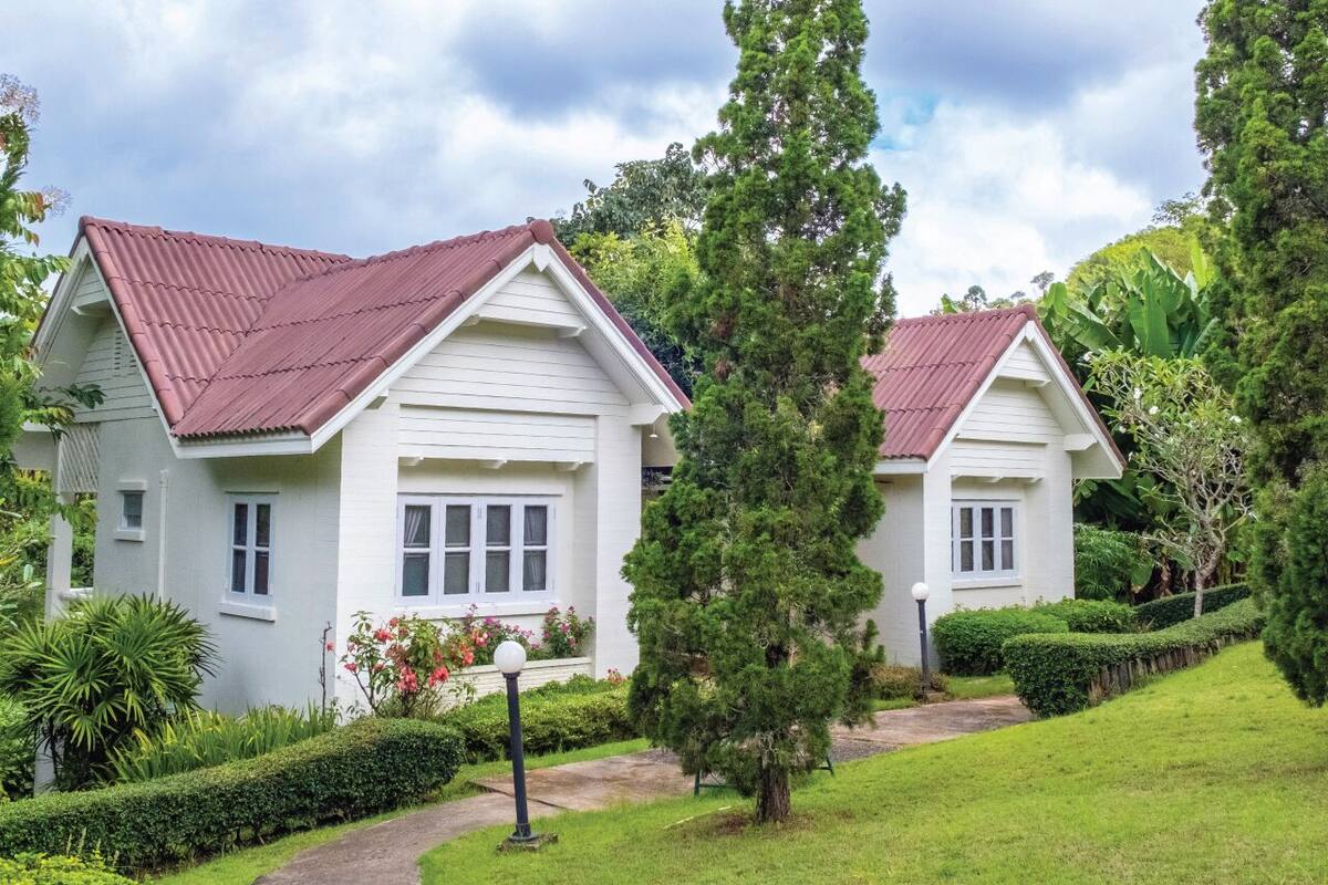 A row of two-story houses with red roofs and white walls, surrounded by well-maintained gardens and trees.