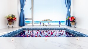 A pool with rose petals and candles, a view of the beach, and a balcony with blue curtains.