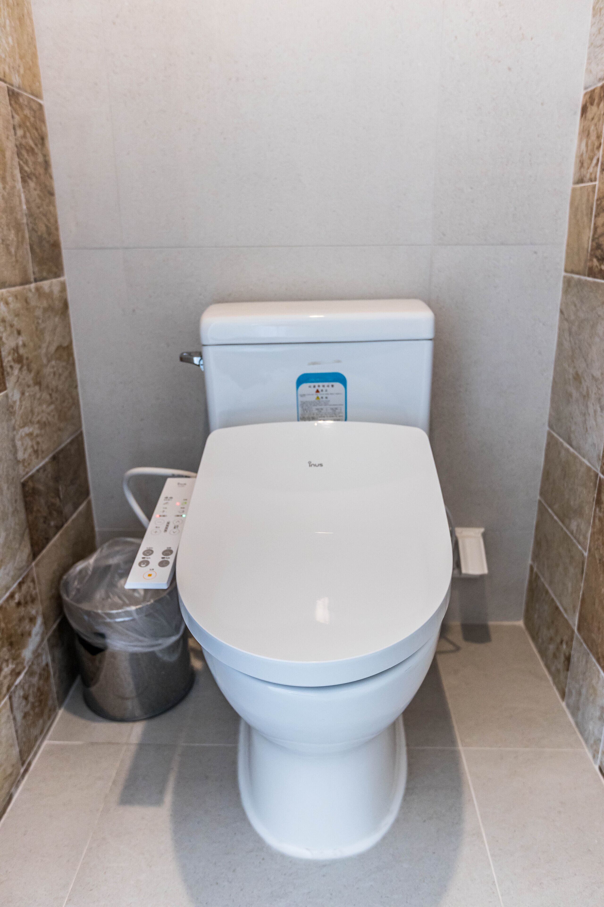 A white toilet with a control panel, a trash bin, and a wall-mounted flush handle.