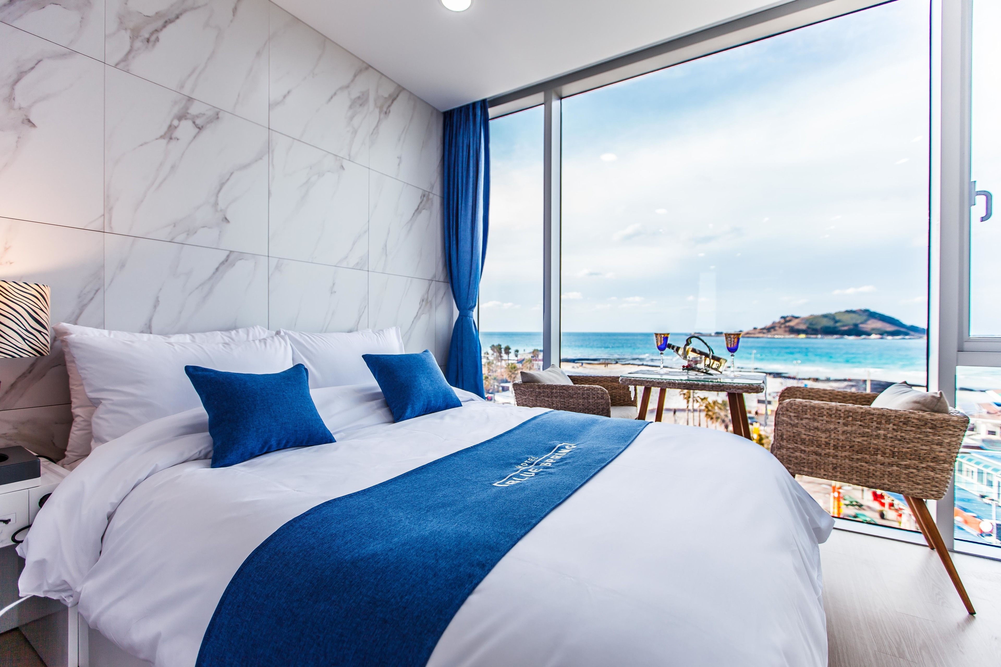A hotel room with a large bed, a view of the beach, and a balcony with wicker furniture.