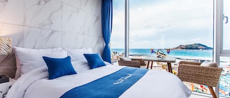 A hotel room with a large bed, a view of the beach, and a balcony with wicker furniture.