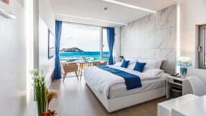 A modern hotel room with a large bed, a desk, and a view of the ocean.