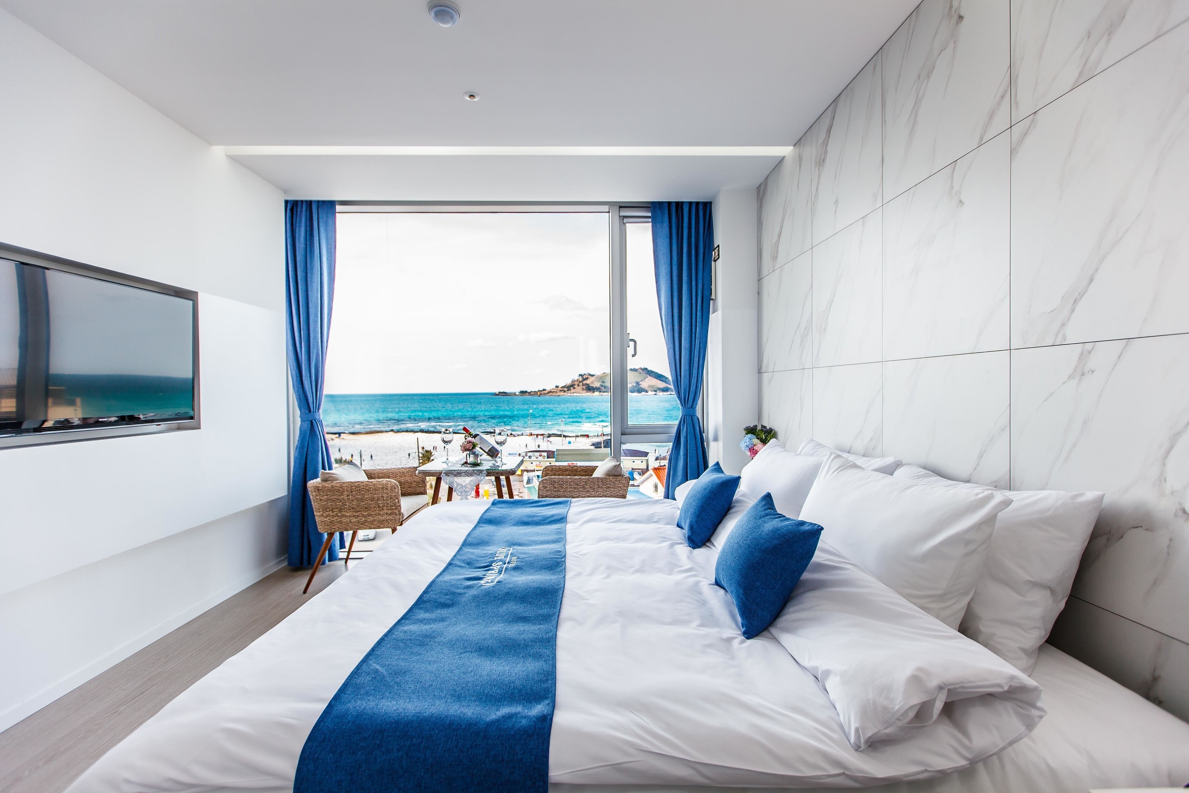 Een hotelkamer met een groot bed, een televisie en uitzicht op het strand.