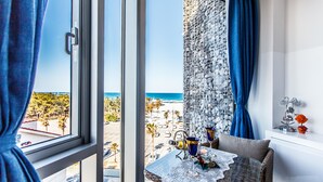 A room with a large window, a table with a lace tablecloth, and a view of the beach.