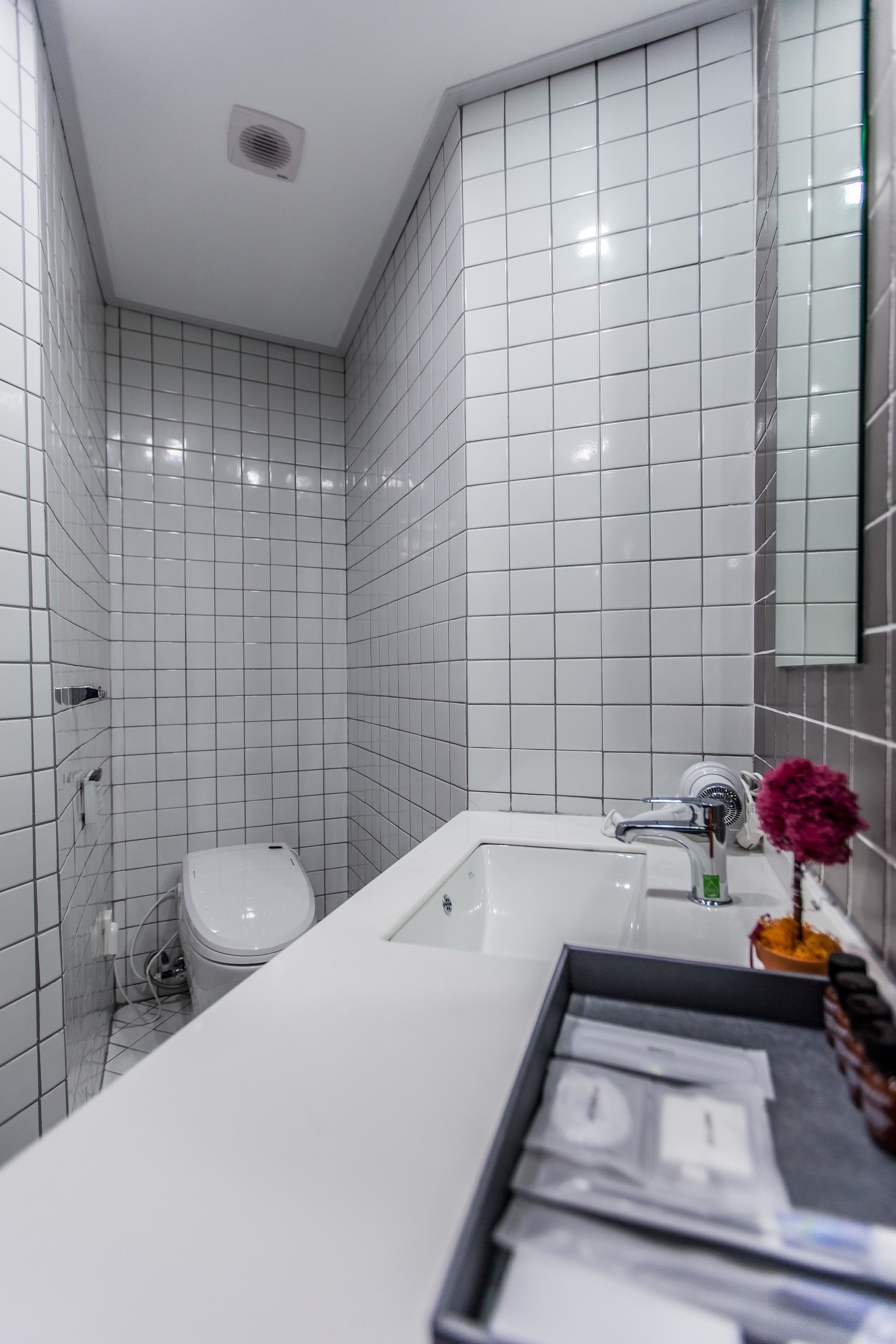 Un baño moderno con azulejos blancos, un lavamanos blanco y un inodoro.