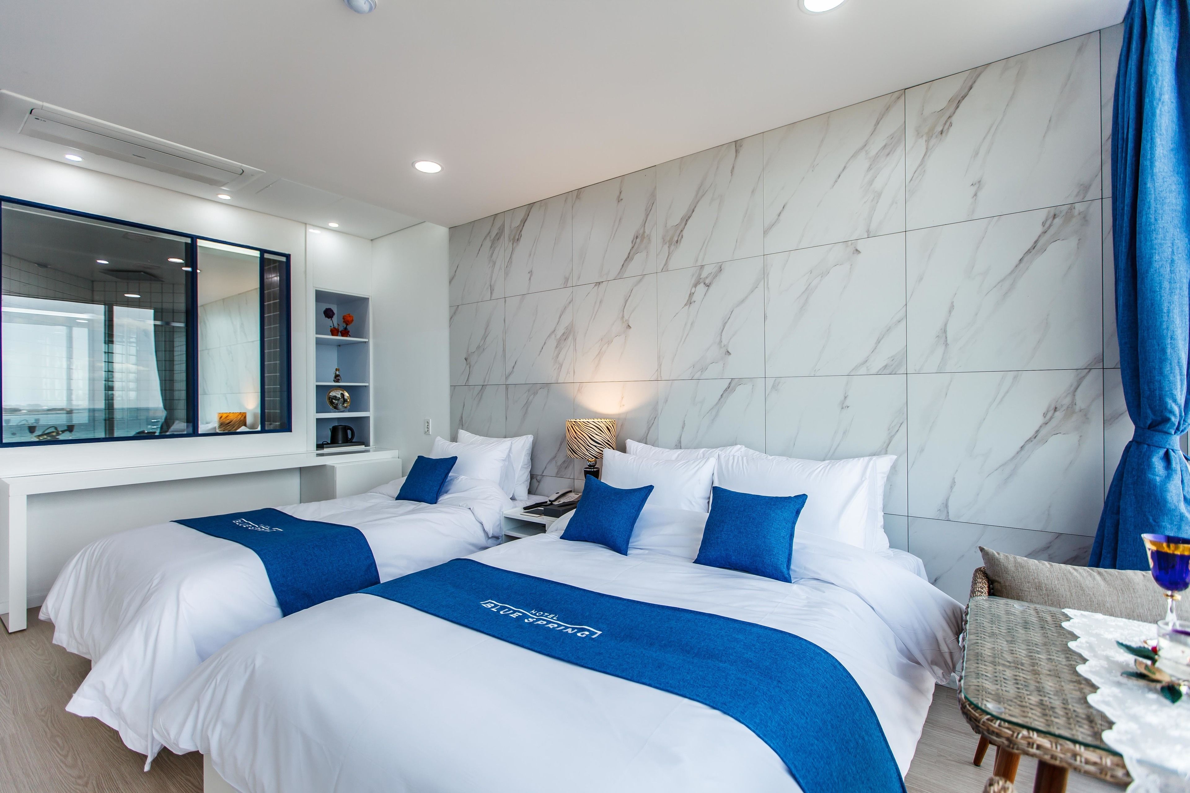 A hotel room with two beds, a large mirror, a marble wall, and a small table with a glass.