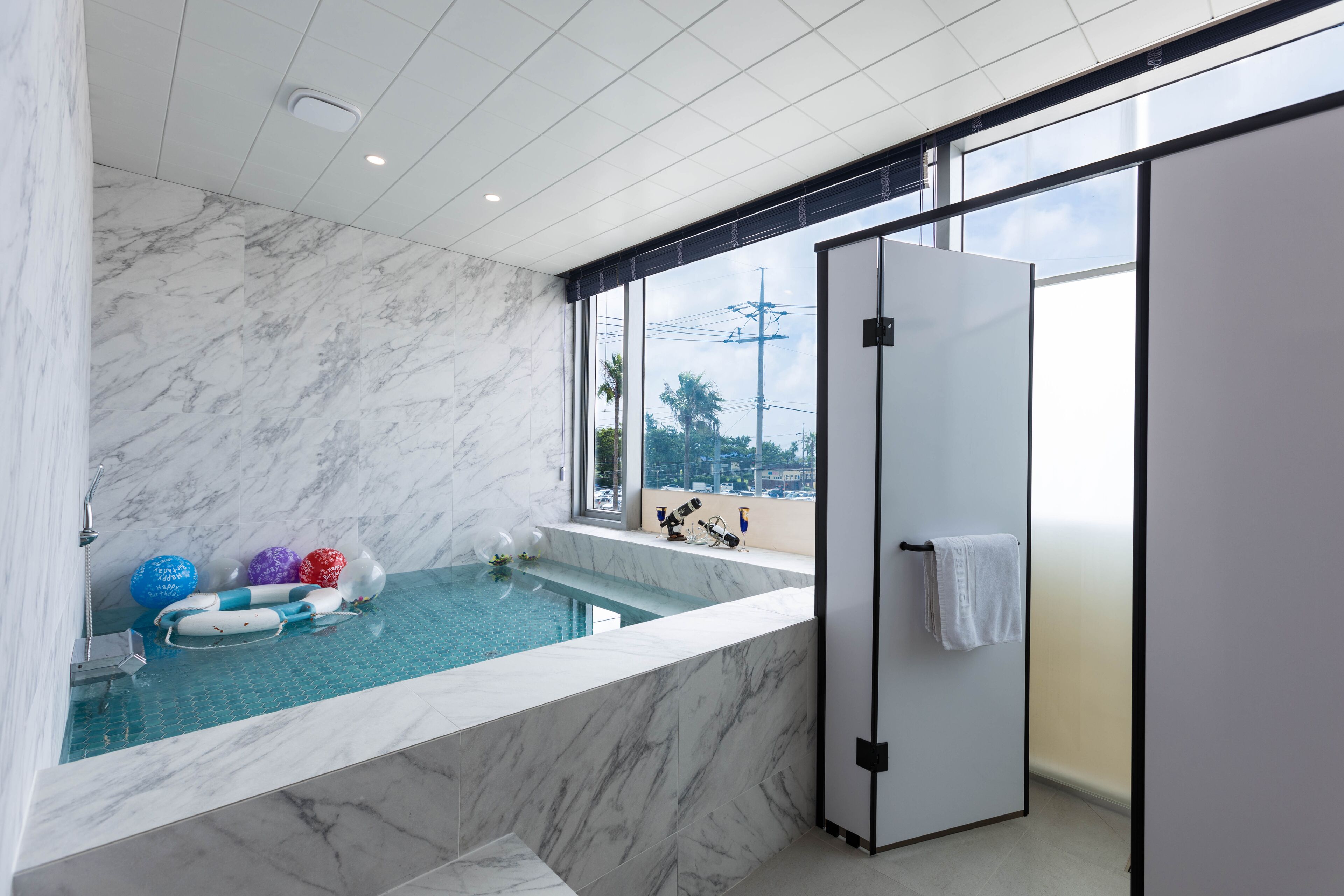 A modern bathroom with a marble floor, a bathtub, and a large window offering a view of the city.