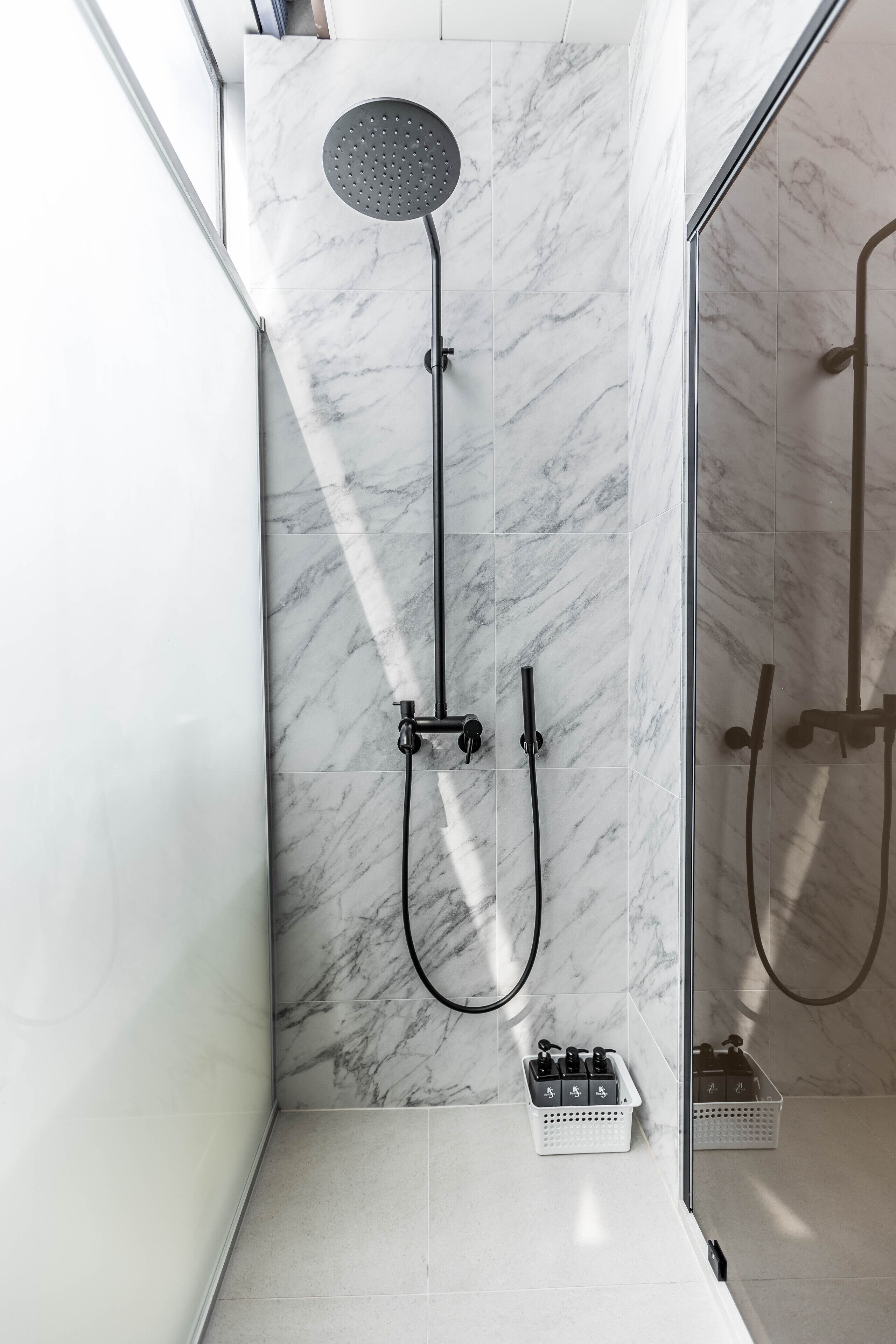 A modern shower with a handheld showerhead and a wall-mounted faucet, marble tiles, and a glass shower enclosure.