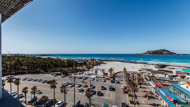 A parking lot with cars, a beach, and a mountain in the distance.
