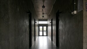 Um corredor comprido e estreito, com paredes de concreto e piso de azulejos, que leva a uma saída iluminada.