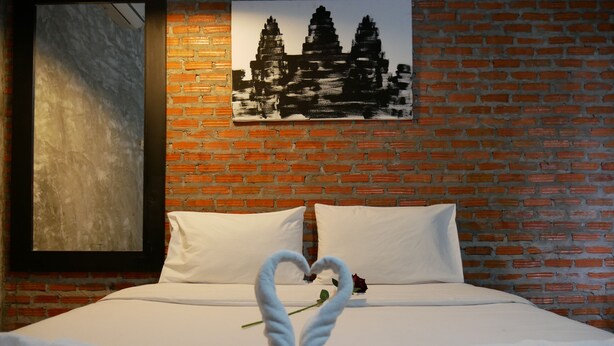 Quarto de hotel com parede de tijolos, cama com roupa de cama branca e arranjo de toalha em formato de coração sobre a cama.