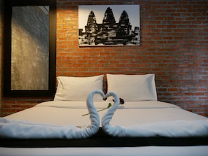 Habitación de hotel con pared de ladrillo, una cama con ropa de cama blanca y una disposición de toallas en forma de corazón sobre la cama.