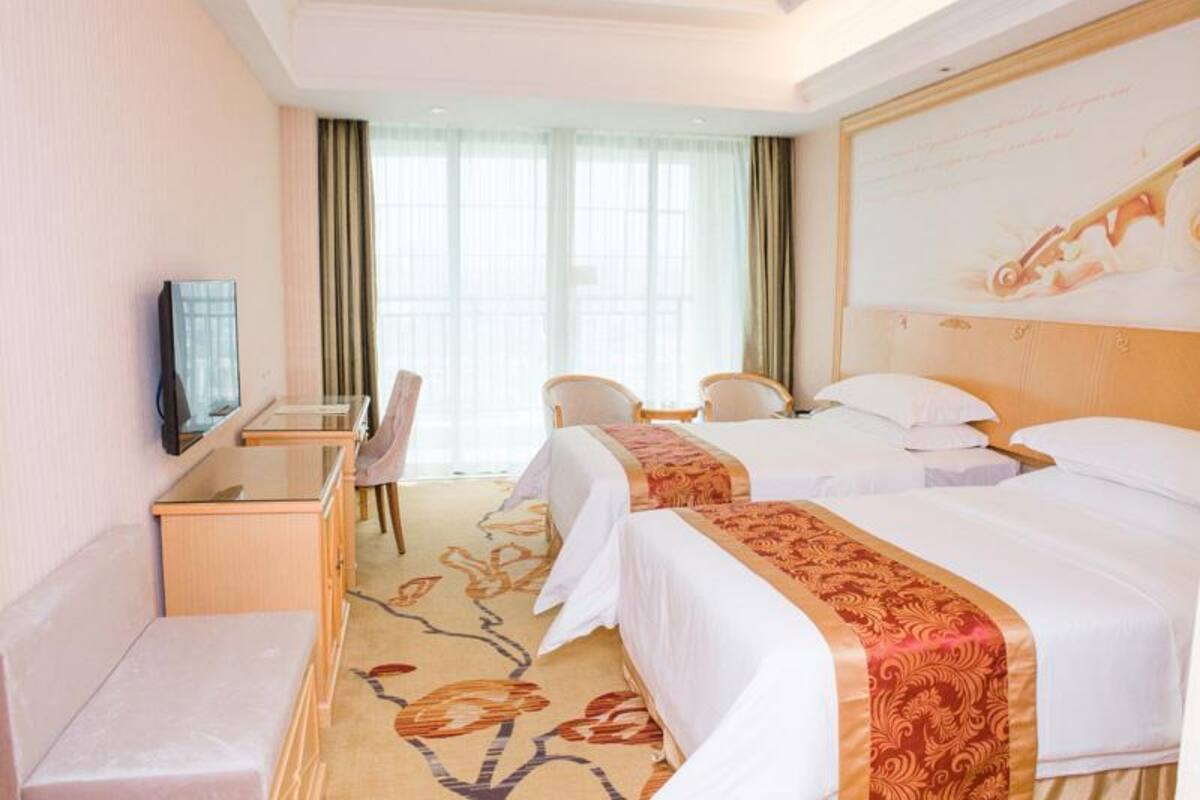 A hotel room with two beds, a desk, a chair, and a television.