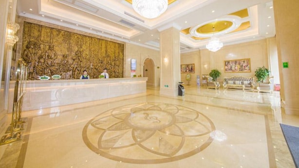 A hotel lobby with a reception desk, a large decorative wall, a chandelier, and a floral floor design. - Vienna Hotel Qingyuan Taihe Ancient Cave (Qingyuan)