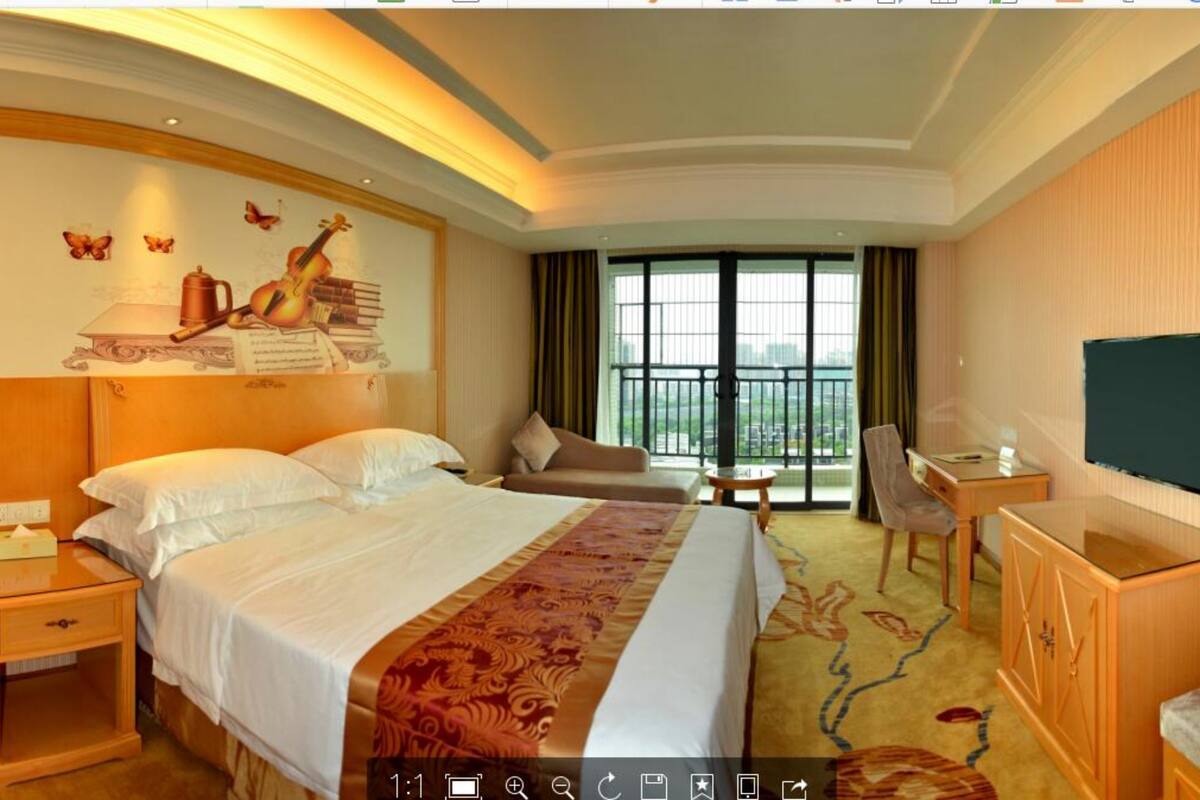 A hotel room with a large bed, a desk, a chair, a TV, and a window with a view.