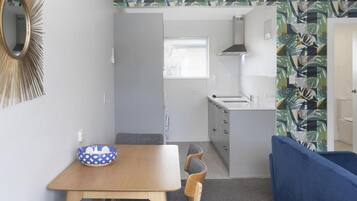 Une cuisine compacte avec un plan de travail blanc, un évier et une cuisinière. On y trouve également un coin repas avec une table et des chaises en bois.