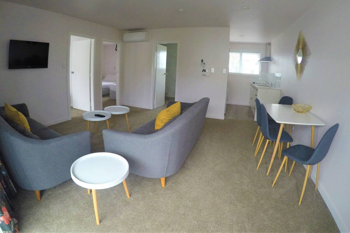 A modern living room with grey sofas, a white dining table with blue chairs, and a small white side table.