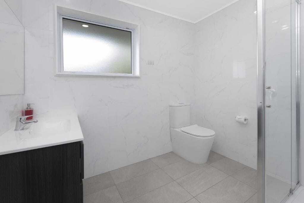 A modern bathroom with a toilet, a shower enclosure, and a window.