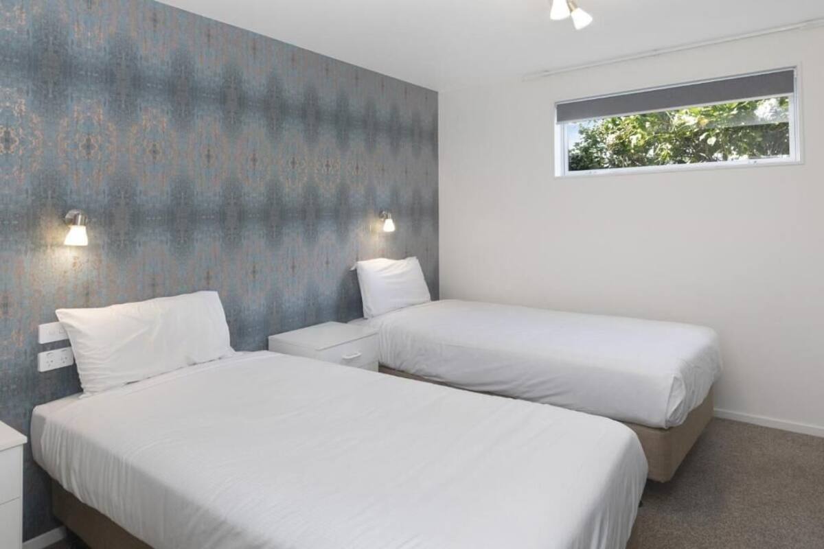 A bedroom with two beds, a window, and wall-mounted lights.