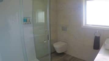 Een moderne badkamer met een glazen douchecabine, toilet en wastafel.