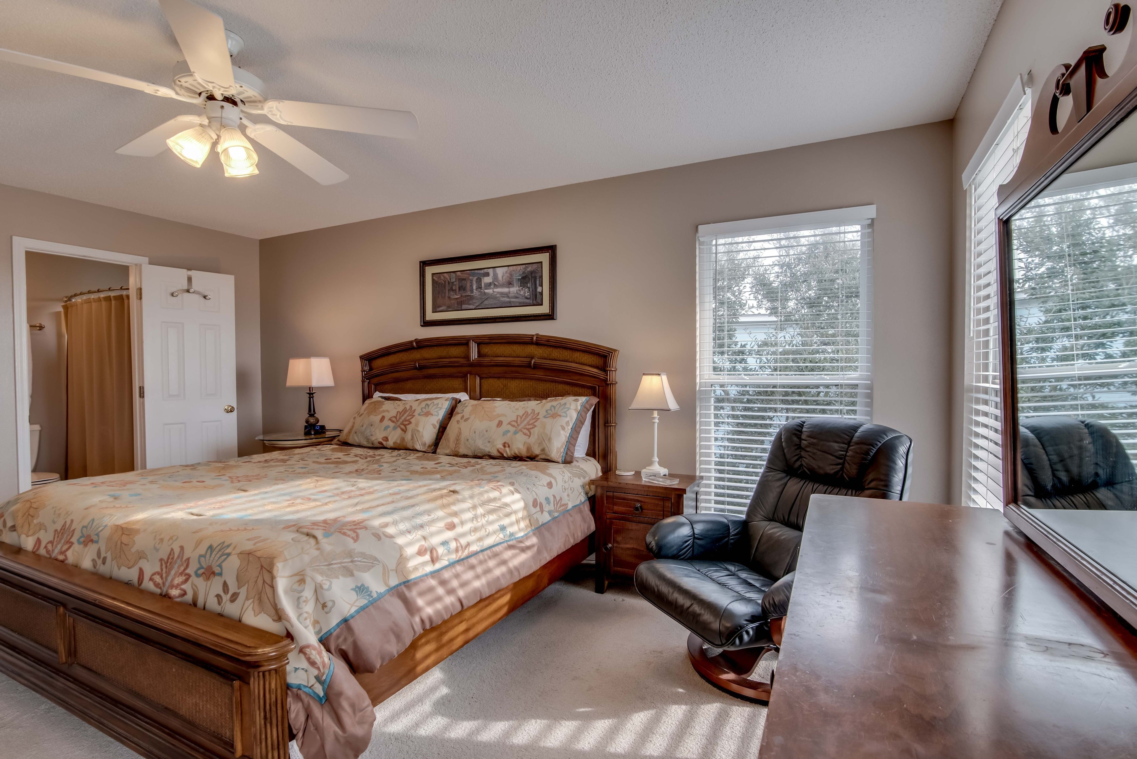 A bedroom with a bed, bedside lamps, a chair, a desk, and a ceiling fan.