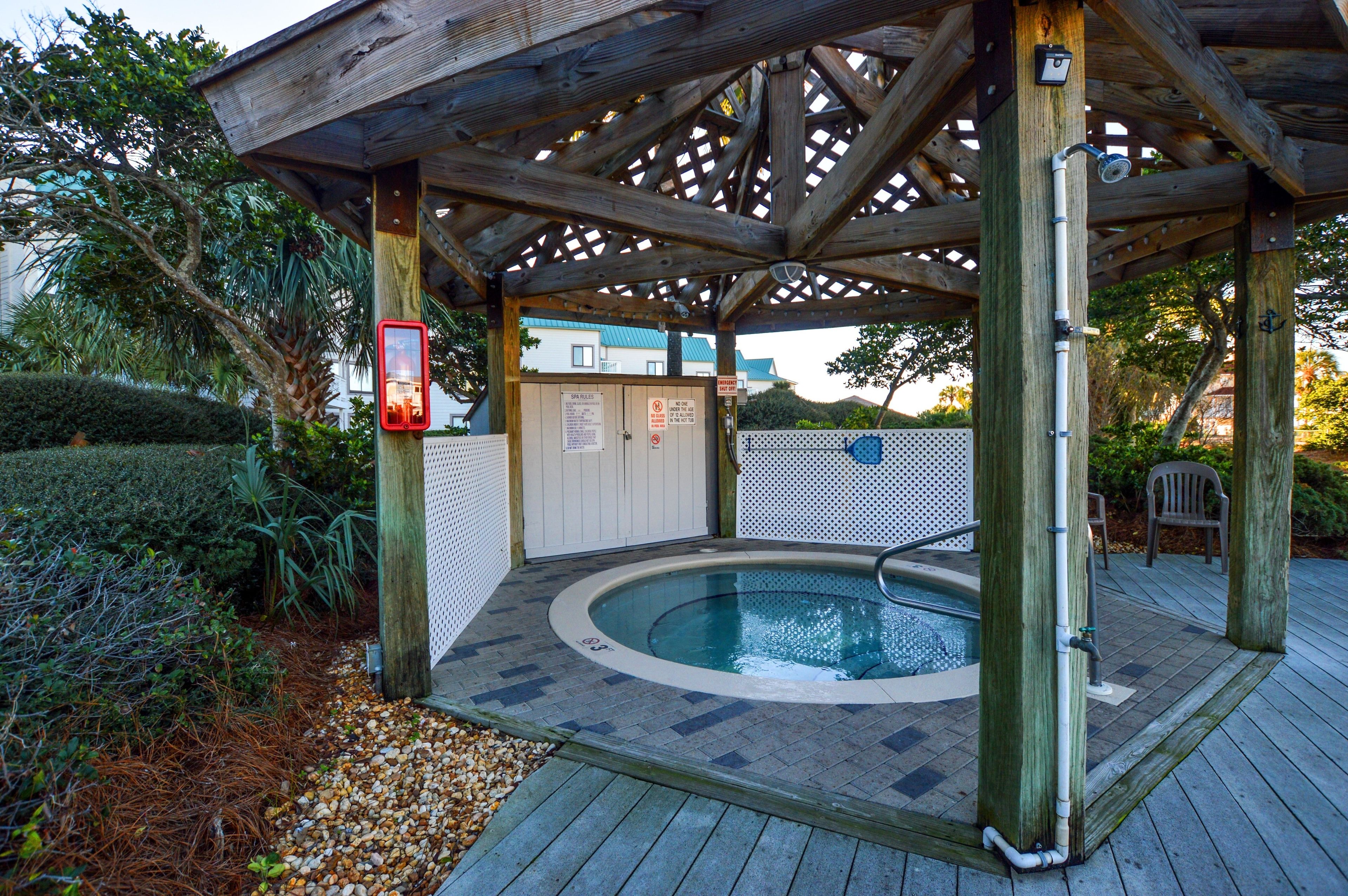 A wooden deck with a hot tub, surrounded by a wooden pergola and a white fence.